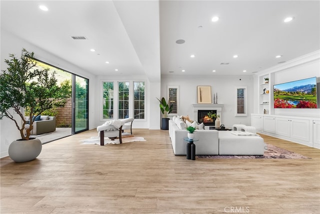 living room with recessed lighting, visible vents, built in features, light wood-type flooring, and a glass covered fireplace