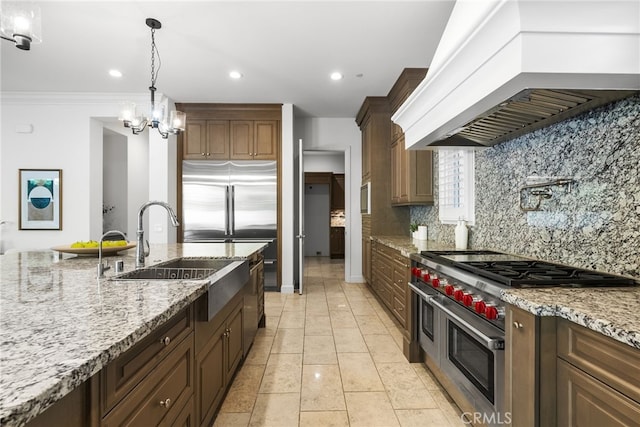 kitchen featuring light stone counters, pendant lighting, custom exhaust hood, high end appliances, and tasteful backsplash