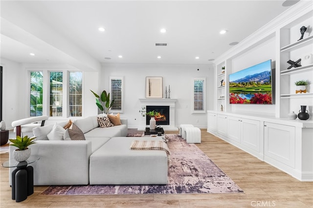 living room with built in features, recessed lighting, visible vents, light wood-style flooring, and a warm lit fireplace