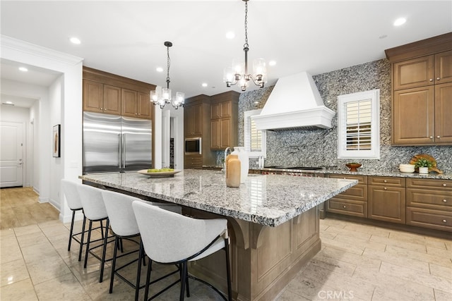 kitchen featuring built in appliances, premium range hood, a kitchen bar, and a large island with sink