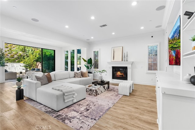 living area with light wood-type flooring, recessed lighting, visible vents, and a glass covered fireplace