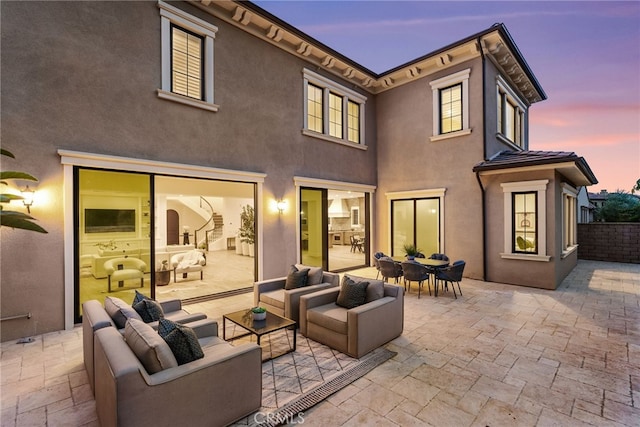 back of property at dusk featuring outdoor dining space, outdoor lounge area, a patio, and stucco siding