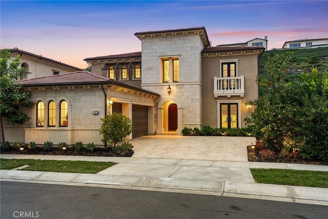 view of front of home featuring an attached garage, concrete driveway, stone siding, and a balcony