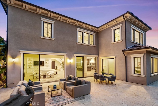 back of property at dusk featuring an outdoor hangout area, outdoor dining area, a patio area, and stucco siding