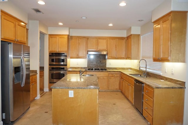 kitchen featuring appliances with stainless steel finishes, a center island with sink, light stone counters, and sink