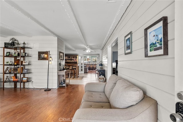 living room with beam ceiling, ceiling fan, hardwood / wood-style floors, and wood walls