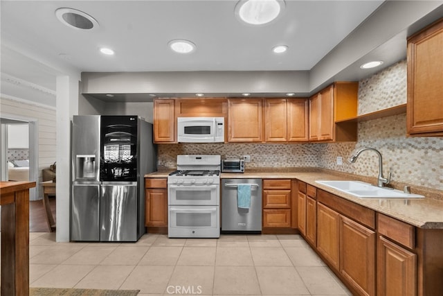 kitchen featuring sink, tasteful backsplash, light stone counters, light tile patterned floors, and appliances with stainless steel finishes