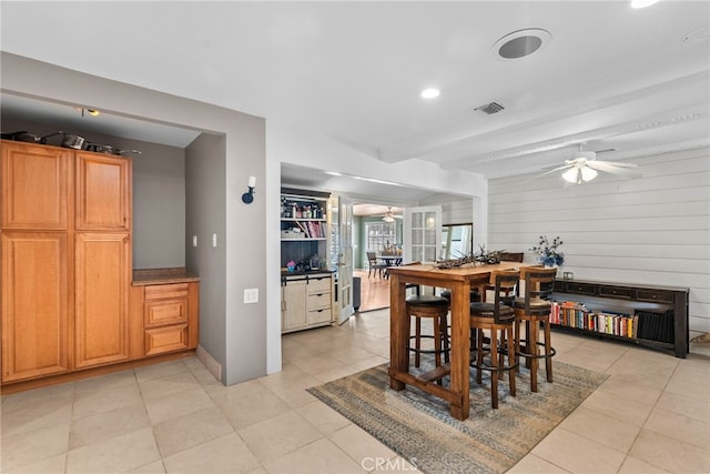 dining space featuring beam ceiling, light tile patterned floors, ceiling fan, and wood walls