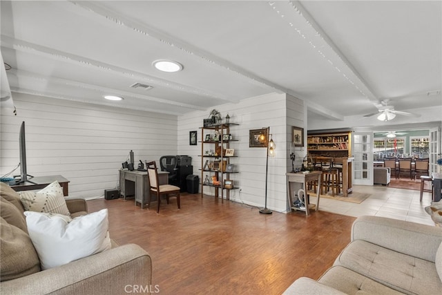 living room featuring ceiling fan, hardwood / wood-style floors, beamed ceiling, and wooden walls