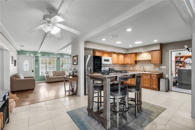 kitchen featuring backsplash, ceiling fan, beam ceiling, light hardwood / wood-style flooring, and a breakfast bar area