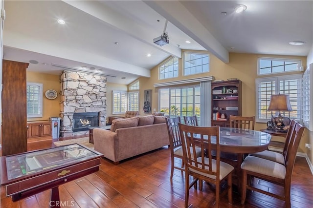 dining area featuring vaulted ceiling with beams, dark hardwood / wood-style flooring, a healthy amount of sunlight, and a stone fireplace