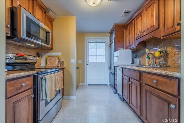 kitchen with appliances with stainless steel finishes, tasteful backsplash, sink, light tile patterned floors, and stone countertops