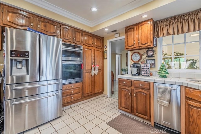 kitchen featuring appliances with stainless steel finishes, light tile patterned floors, tile counters, and ornamental molding