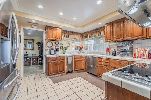 kitchen featuring tile counters, ventilation hood, crown molding, decorative backsplash, and appliances with stainless steel finishes