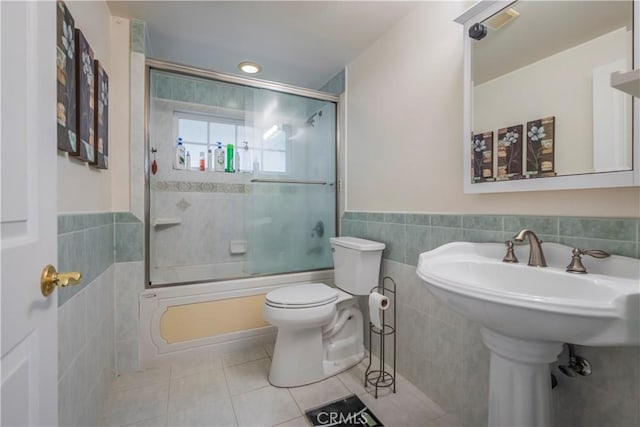 bathroom with tile patterned flooring, toilet, tile walls, and bath / shower combo with glass door