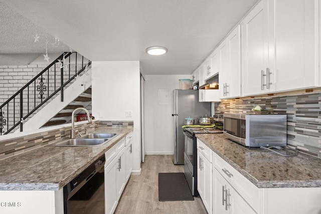 kitchen featuring stainless steel range with electric stovetop, dark stone counters, white cabinets, sink, and light wood-type flooring