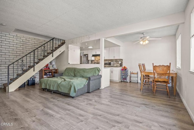 living room featuring ceiling fan, light hardwood / wood-style flooring, brick wall, and a textured ceiling