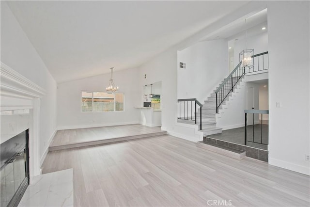 unfurnished living room featuring light wood-type flooring, a fireplace, high vaulted ceiling, and an inviting chandelier