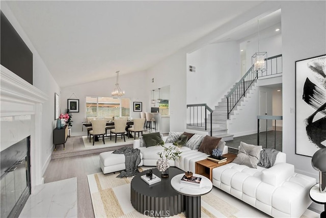 living room featuring light hardwood / wood-style flooring, high vaulted ceiling, a notable chandelier, and a premium fireplace