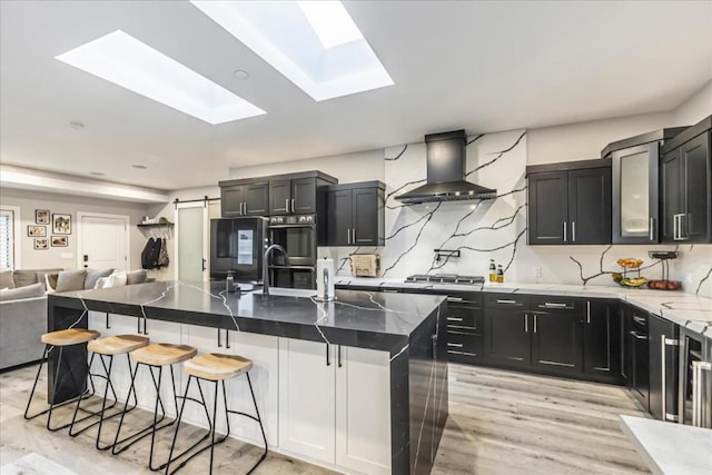 kitchen with a skylight, a kitchen bar, ventilation hood, a kitchen island with sink, and sink