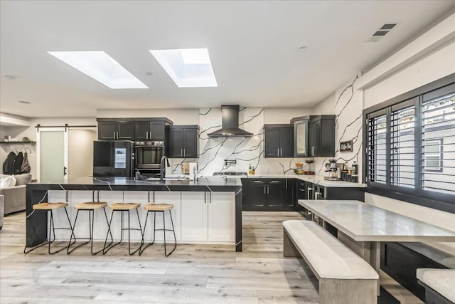 kitchen featuring a barn door, a center island with sink, fridge, a breakfast bar area, and wall chimney exhaust hood