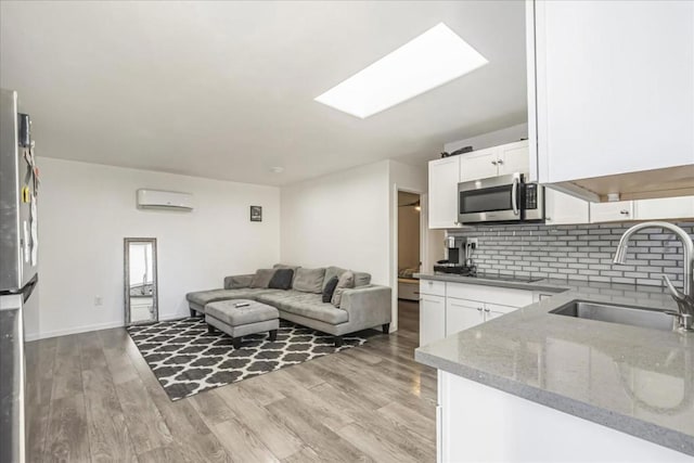 living room with sink, light wood-type flooring, a skylight, and a wall mounted air conditioner