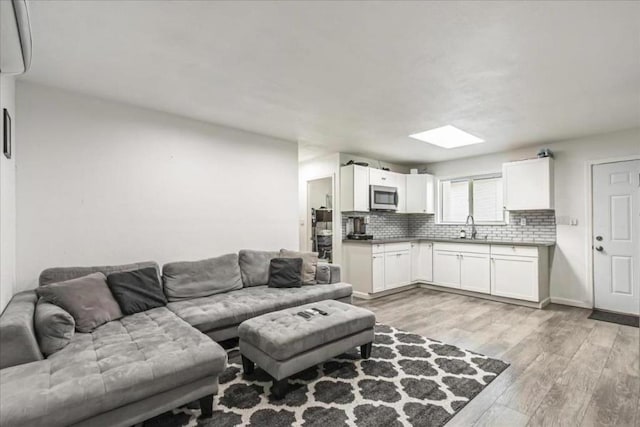 living room with a skylight, sink, and light hardwood / wood-style floors