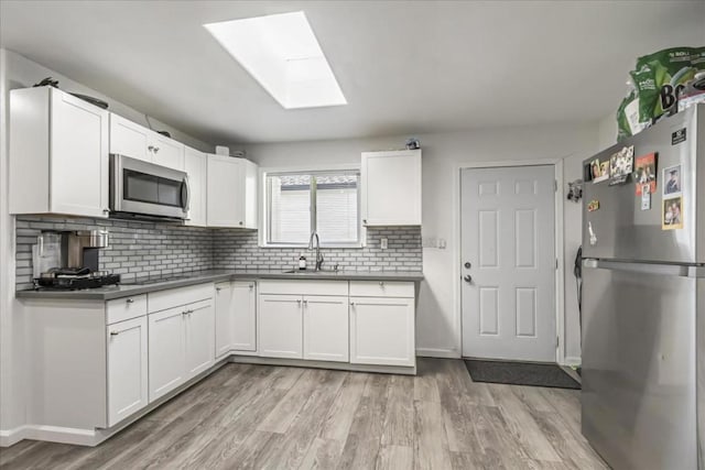 kitchen with a skylight, appliances with stainless steel finishes, and white cabinets