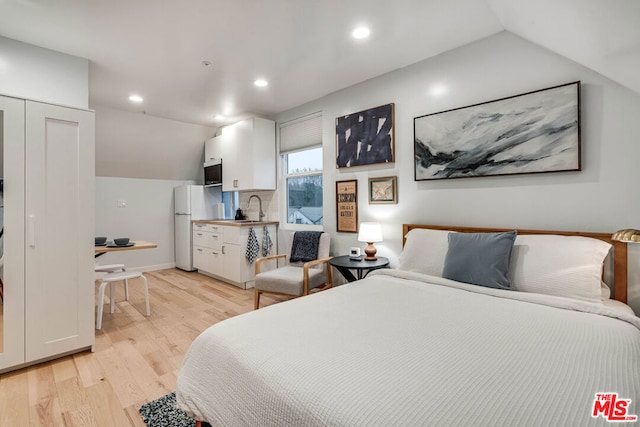 bedroom featuring sink, white refrigerator, light hardwood / wood-style flooring, and lofted ceiling