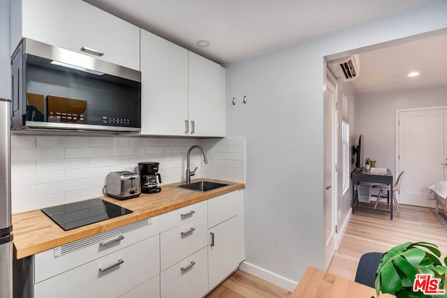 kitchen with a wall mounted AC, sink, white cabinets, black electric cooktop, and wood counters