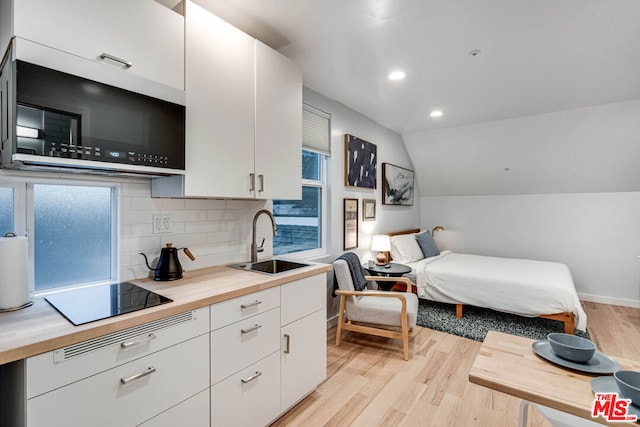 bedroom with light hardwood / wood-style floors, sink, and vaulted ceiling