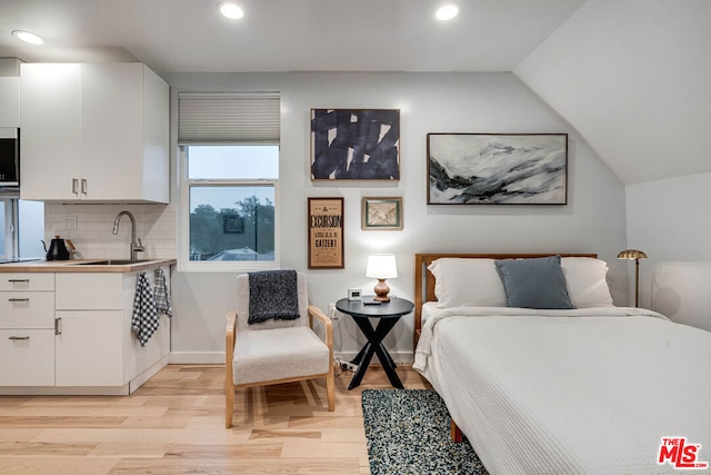 bedroom with sink, light wood-type flooring, and vaulted ceiling