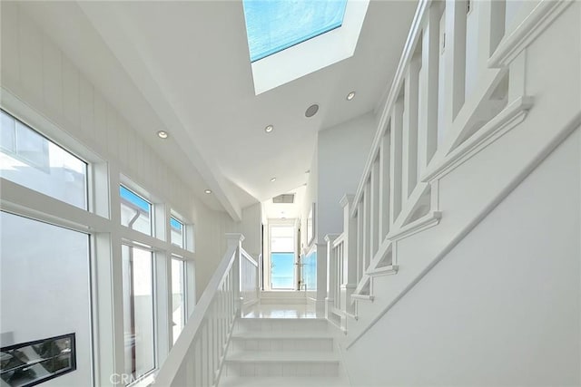 stairway featuring tile patterned flooring, high vaulted ceiling, and a skylight