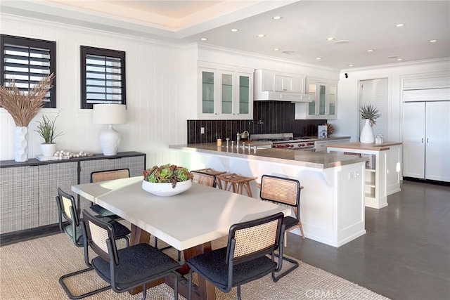 kitchen with a kitchen bar, decorative backsplash, ornamental molding, paneled built in refrigerator, and white cabinetry