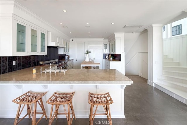 kitchen featuring kitchen peninsula, decorative backsplash, a breakfast bar, and white cabinetry