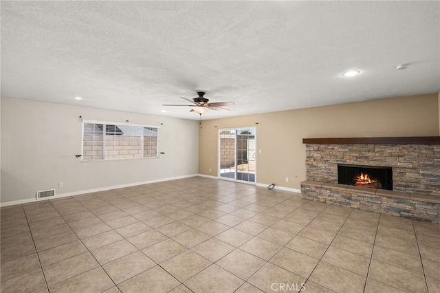 unfurnished living room with a textured ceiling, a stone fireplace, ceiling fan, and light tile patterned flooring