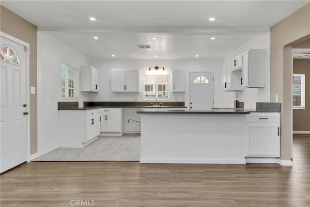 kitchen with white cabinetry, sink, kitchen peninsula, light hardwood / wood-style flooring, and beam ceiling