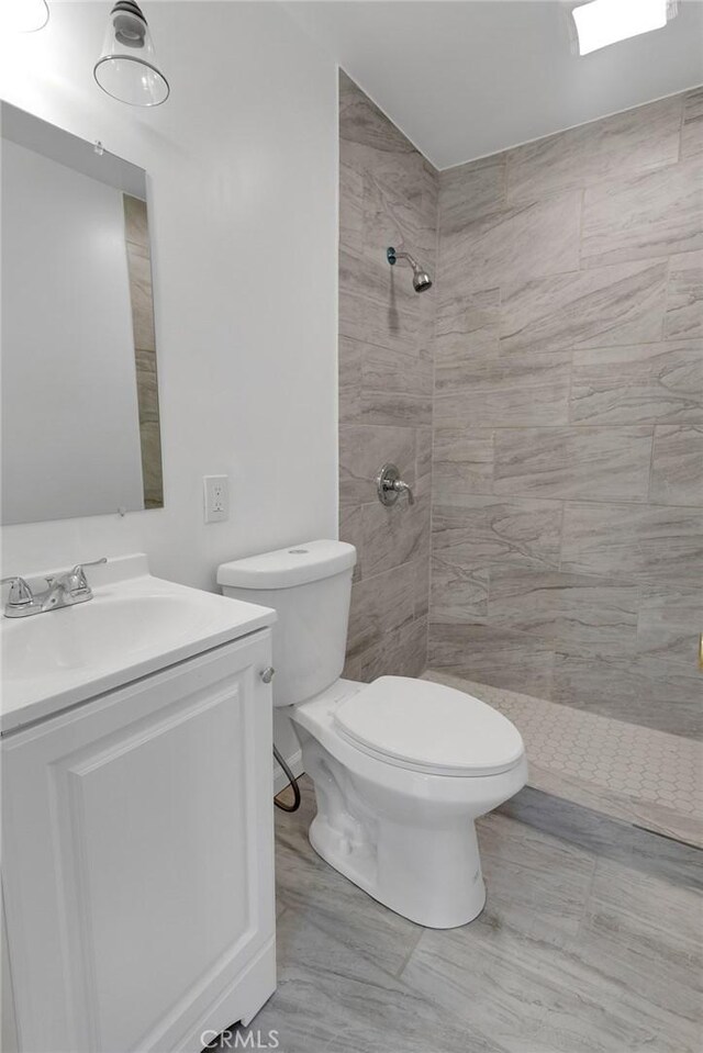 bathroom featuring a tile shower, toilet, and vanity