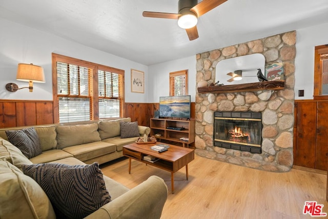 living room with a stone fireplace, wooden walls, light hardwood / wood-style flooring, and ceiling fan