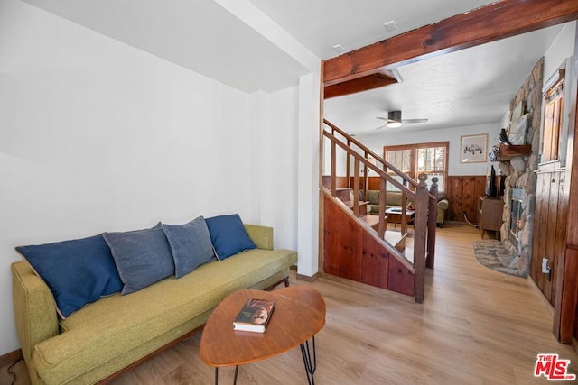 living room with beamed ceiling, ceiling fan, light wood-type flooring, and wooden walls