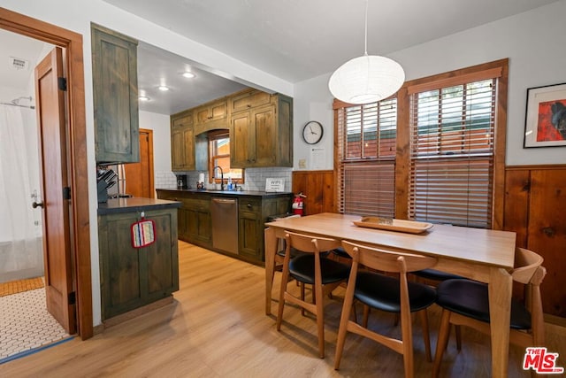 kitchen featuring backsplash, sink, wooden walls, stainless steel dishwasher, and light wood-type flooring