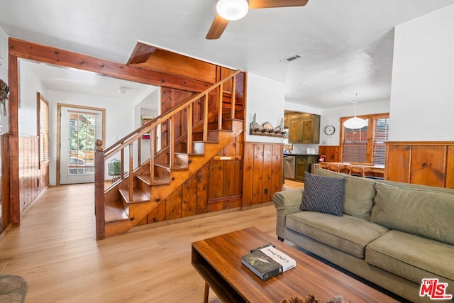 living room featuring ceiling fan, wood walls, and light wood-type flooring