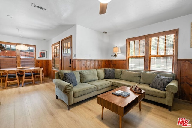 living room with ceiling fan, wooden walls, and light hardwood / wood-style flooring