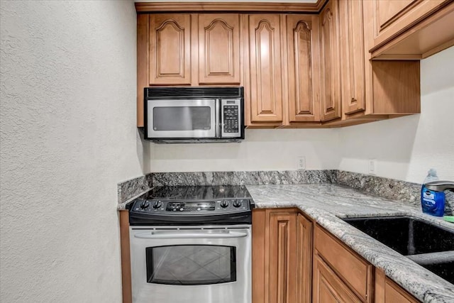 kitchen with sink, light stone counters, and stainless steel appliances