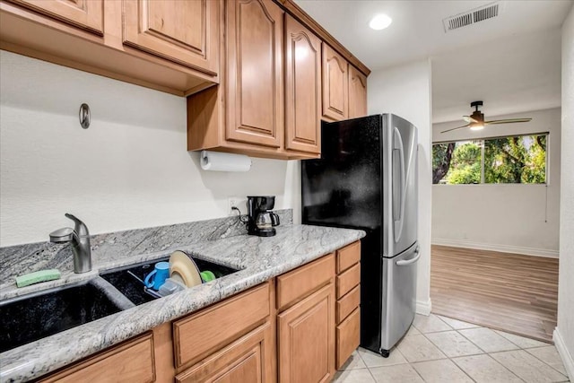 kitchen with ceiling fan, light hardwood / wood-style floors, light stone countertops, and stainless steel refrigerator