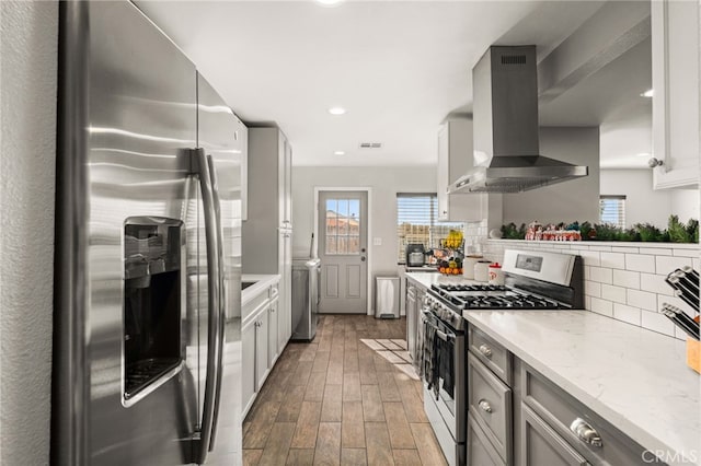 kitchen with backsplash, light stone countertops, appliances with stainless steel finishes, gray cabinetry, and island range hood