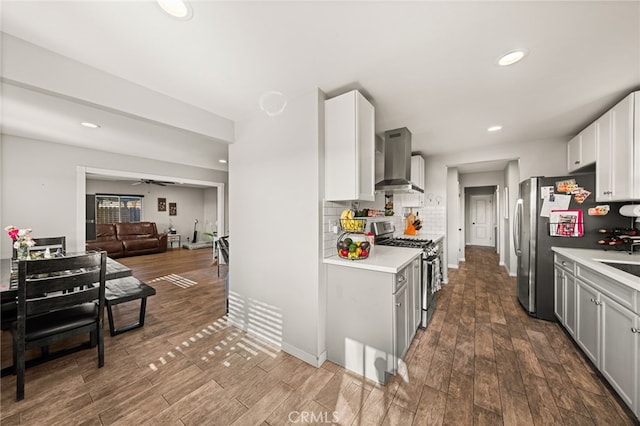 kitchen featuring wall chimney exhaust hood, wood-type flooring, stainless steel appliances, decorative backsplash, and ceiling fan