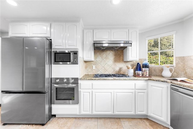 kitchen with white cabinets, light stone countertops, light tile patterned floors, ornamental molding, and stainless steel appliances