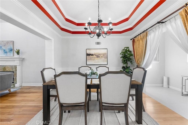 dining space featuring hardwood / wood-style floors, a notable chandelier, a raised ceiling, and crown molding