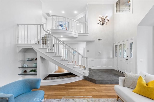 entryway with hardwood / wood-style floors, a notable chandelier, ornamental molding, and a high ceiling